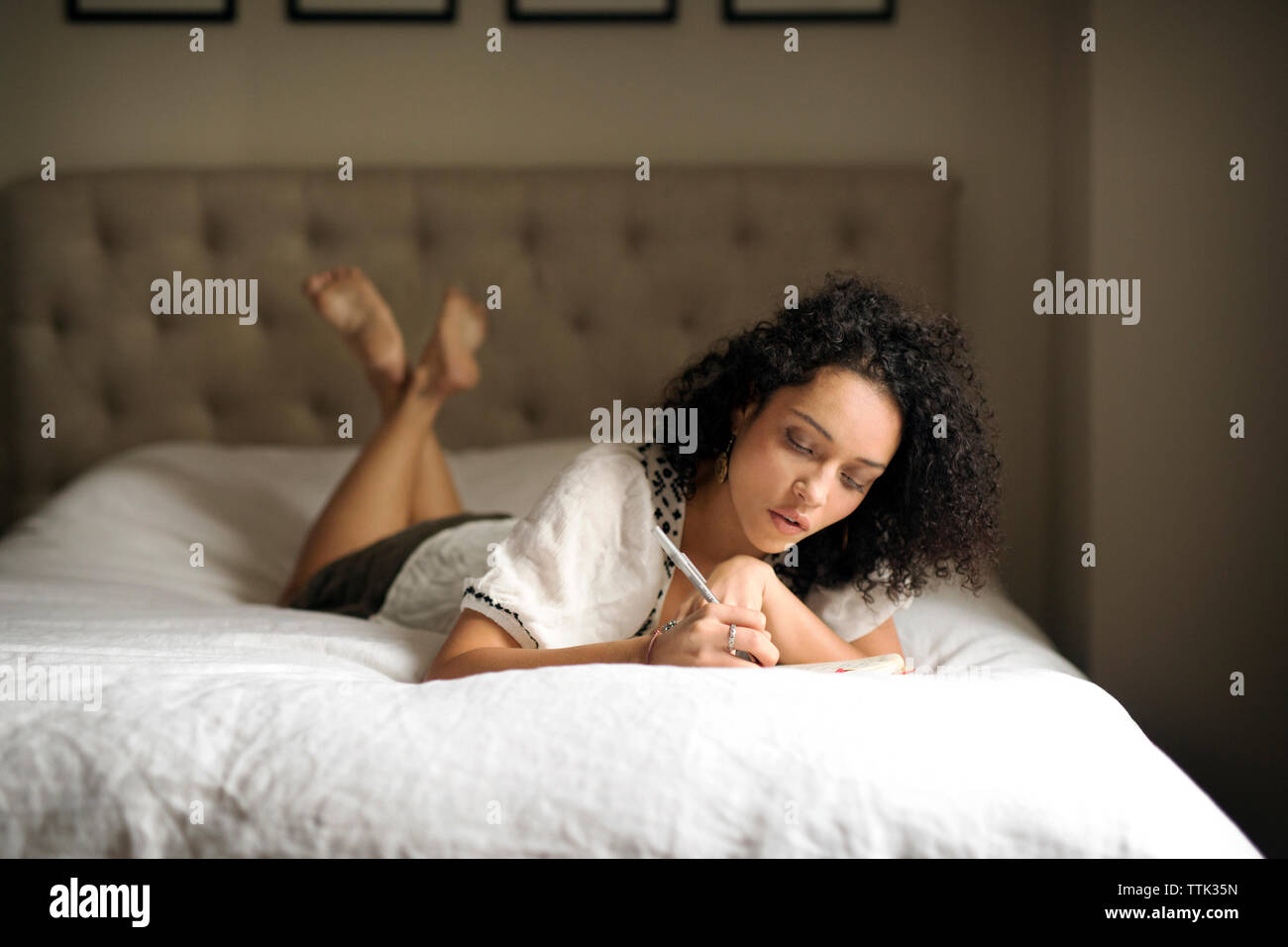 Woman writing on book while relaxing in bedroom Stock Photo - Alamy