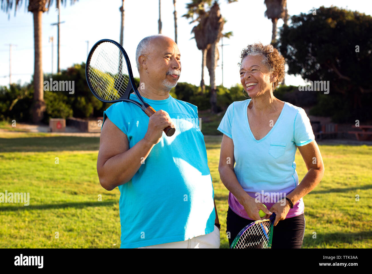 Cheerful friends with rackets talking while standing in park Stock Photo