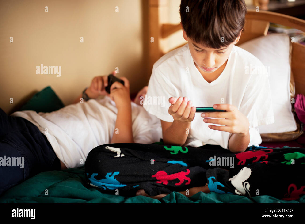 Brothers using phone while resting on bed at home Stock Photo