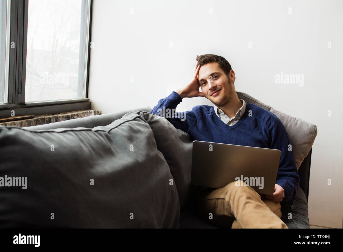 Smiling man using laptop while sitting on sofa at home Stock Photo