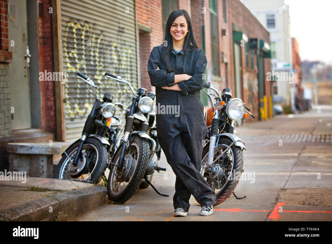 Portrait of happy female mechanic standing against bikes outside shop Stock Photo