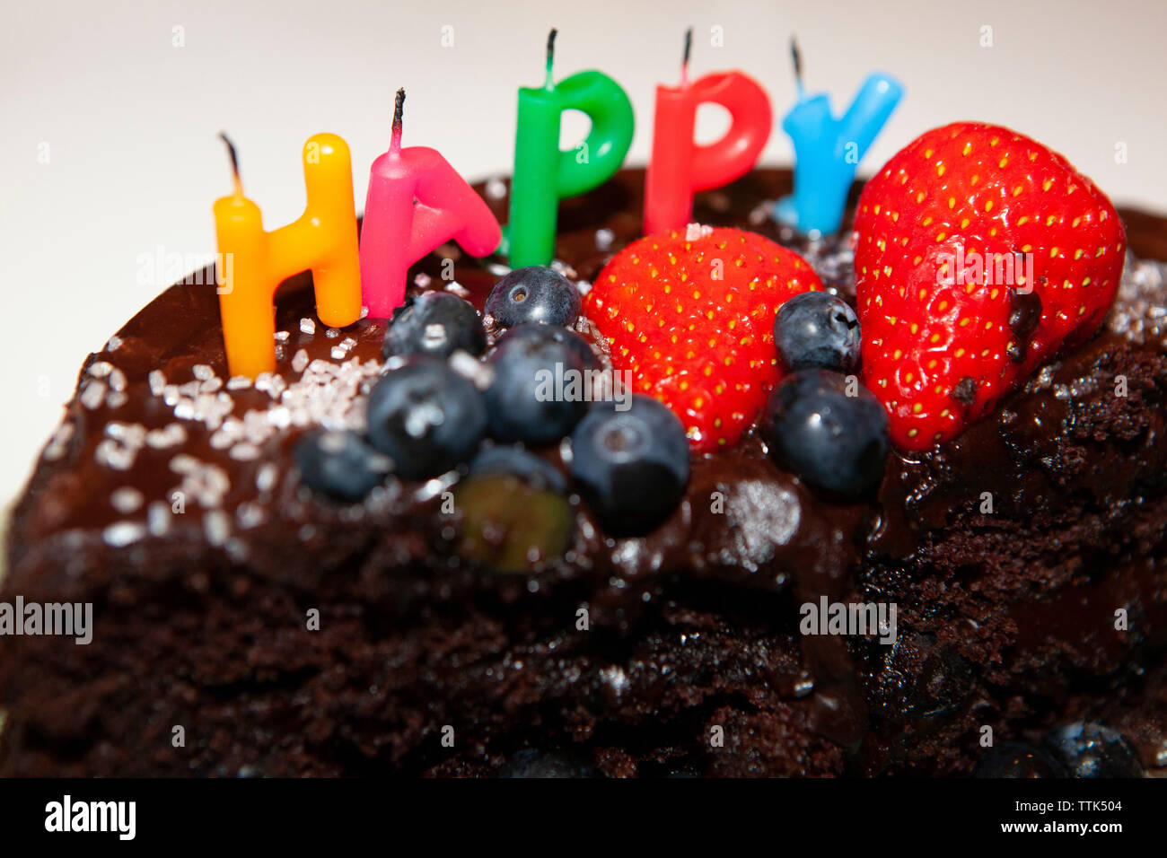 A partly eaten chocolate cake with blown-out candles saying HAPPY. The cake is decorated with blueberries and strawberries, chocolate icing and pink s Stock Photo