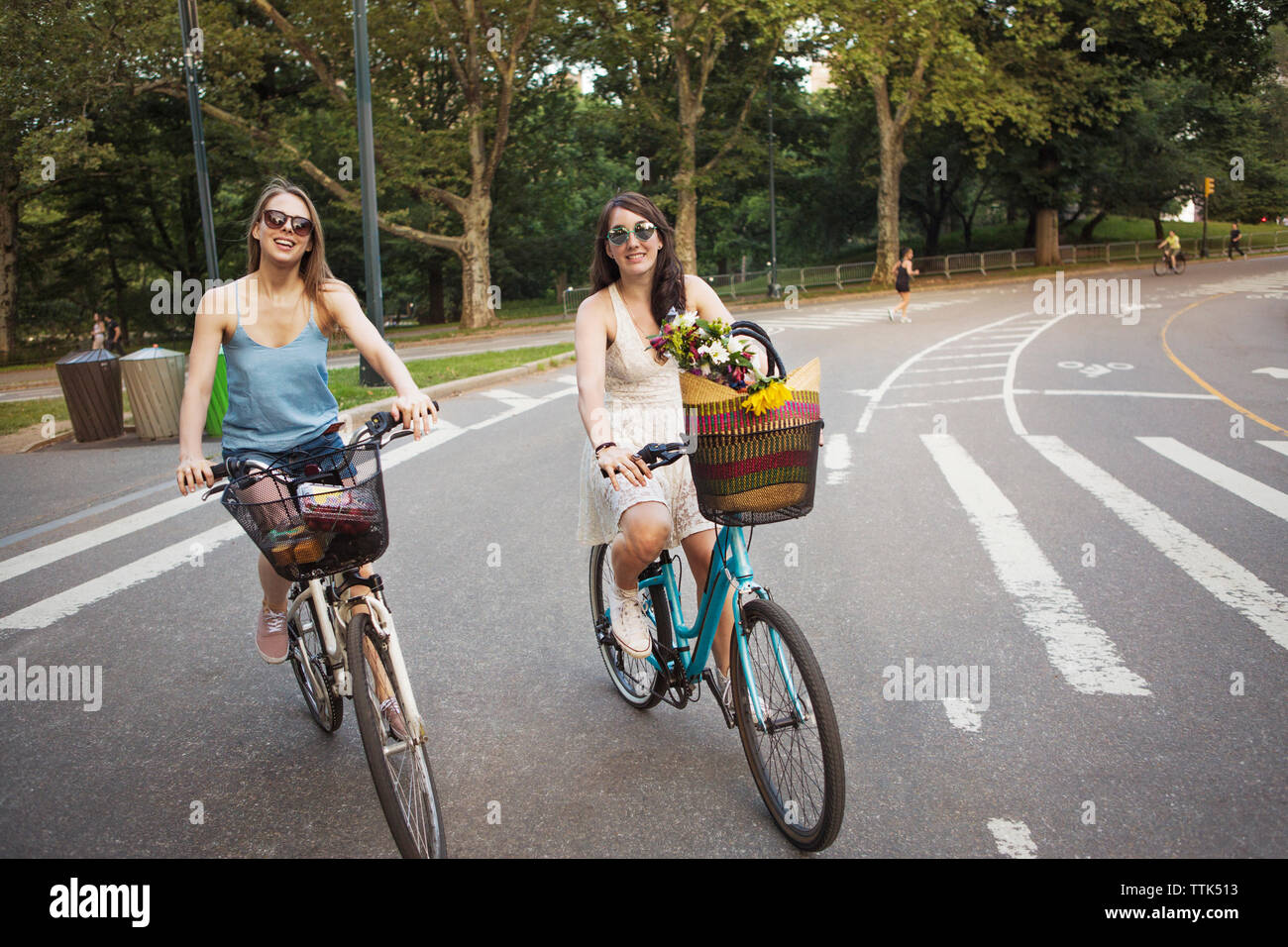 Smiling women cycling on city street against trees Stock Photo