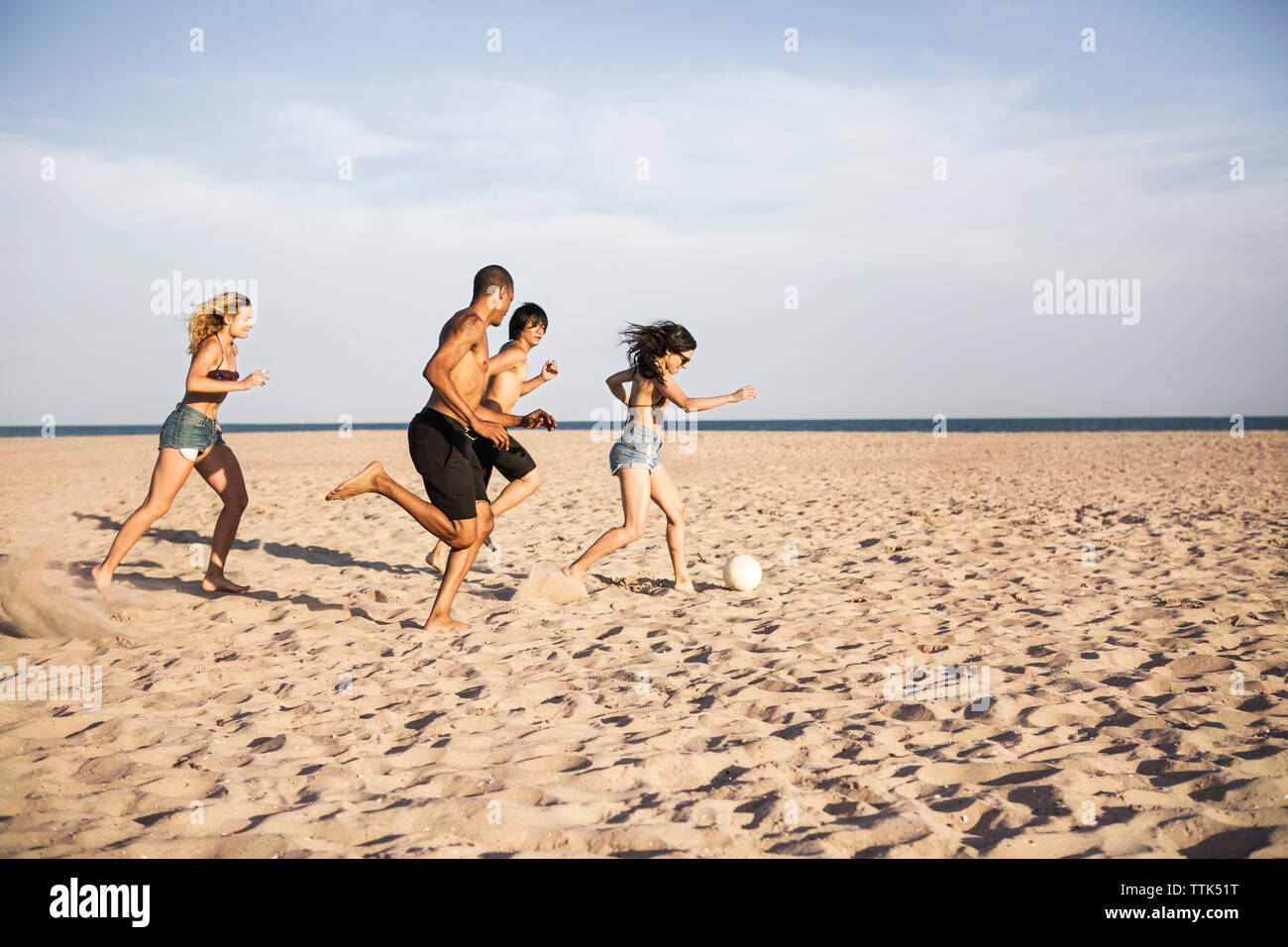 Friends playing soccer on sand at beach against sky Stock Photo