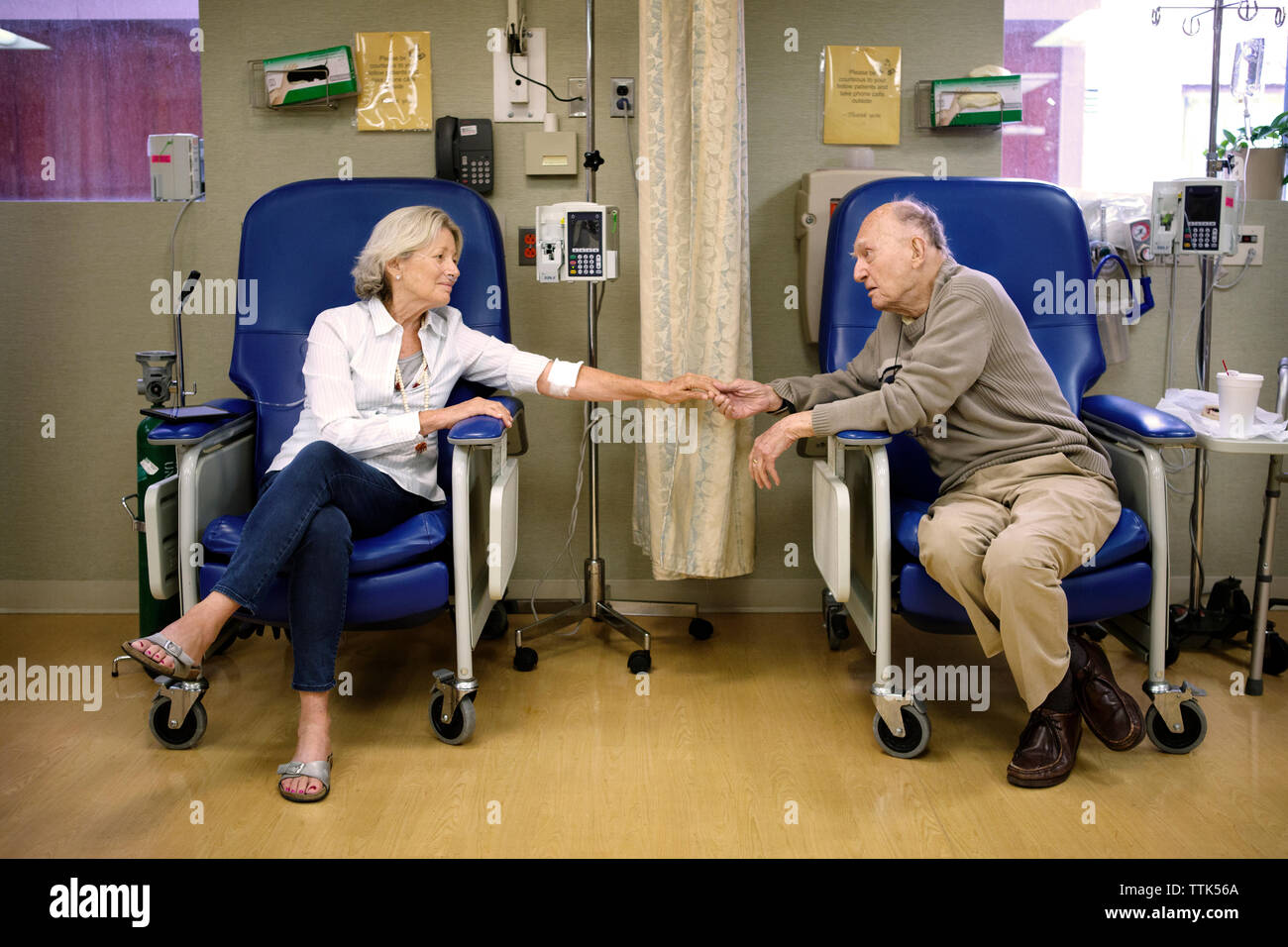 Senior couple holding hands while sitting on chairs in hospital Stock Photo