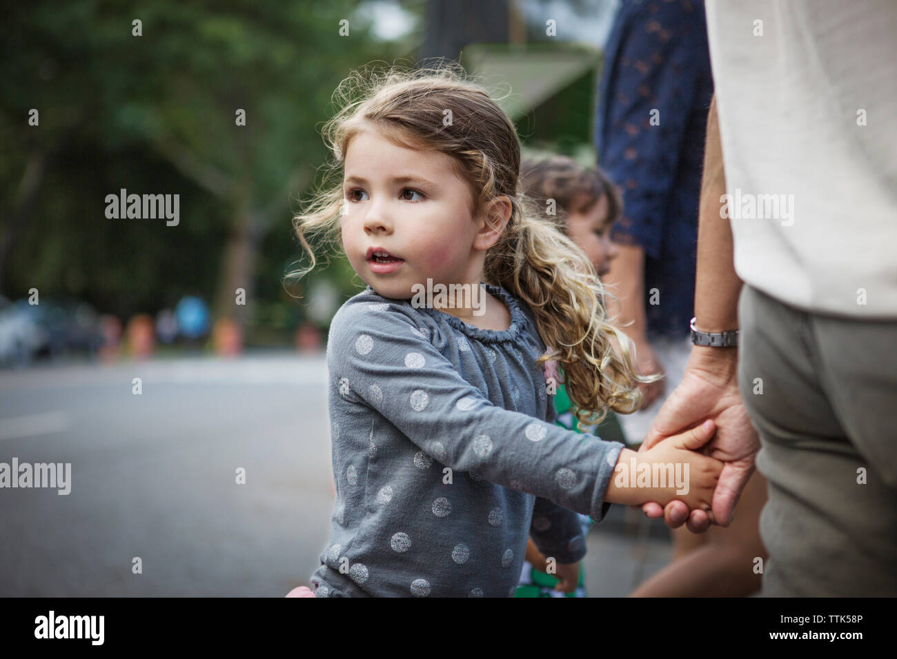 Girl looking away while holding father's hand on street Stock Photo