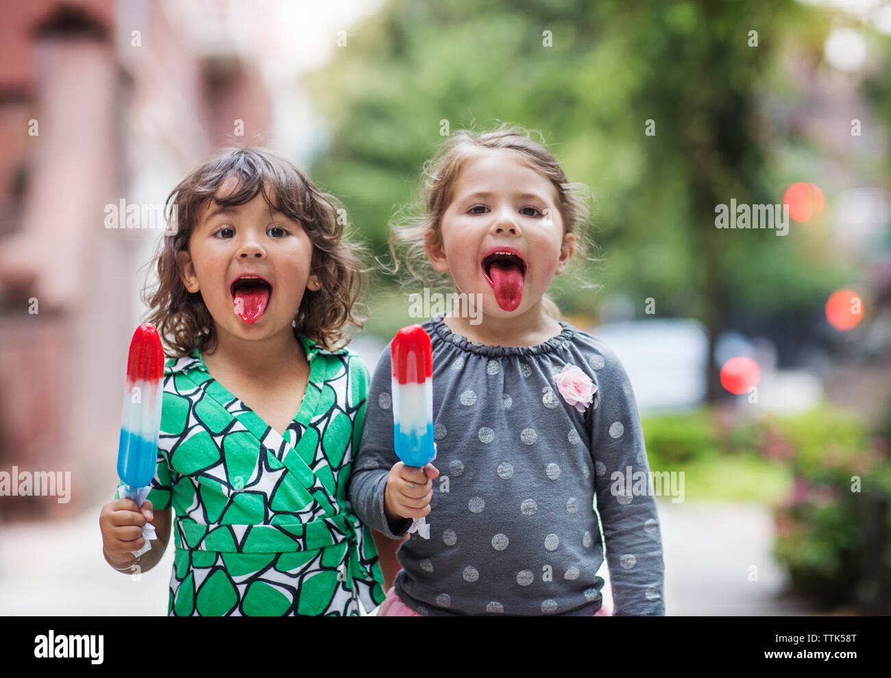 Portrait of girls sticking out tongue while holding ice lollies Stock Photo