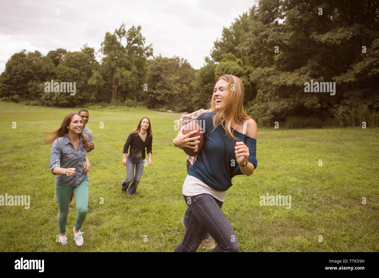 Playful friends chasing woman holding football ball on grassy field Stock Photo