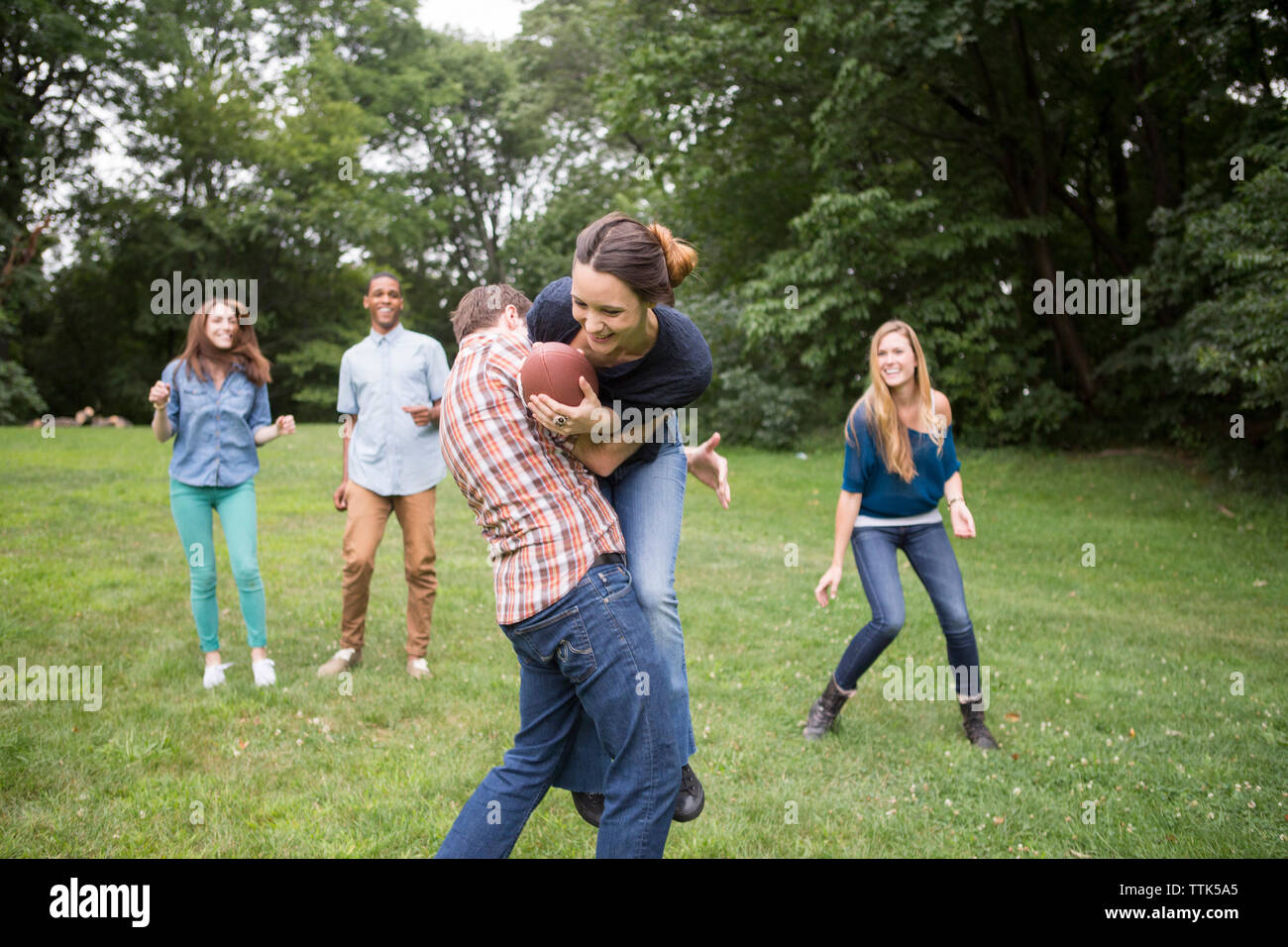 Man defending woman holding football ball while friends watching them on field Stock Photo