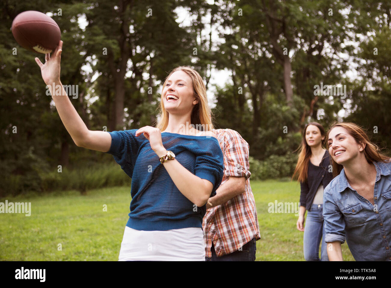 Playful woman throwing football ball while friends running behind on