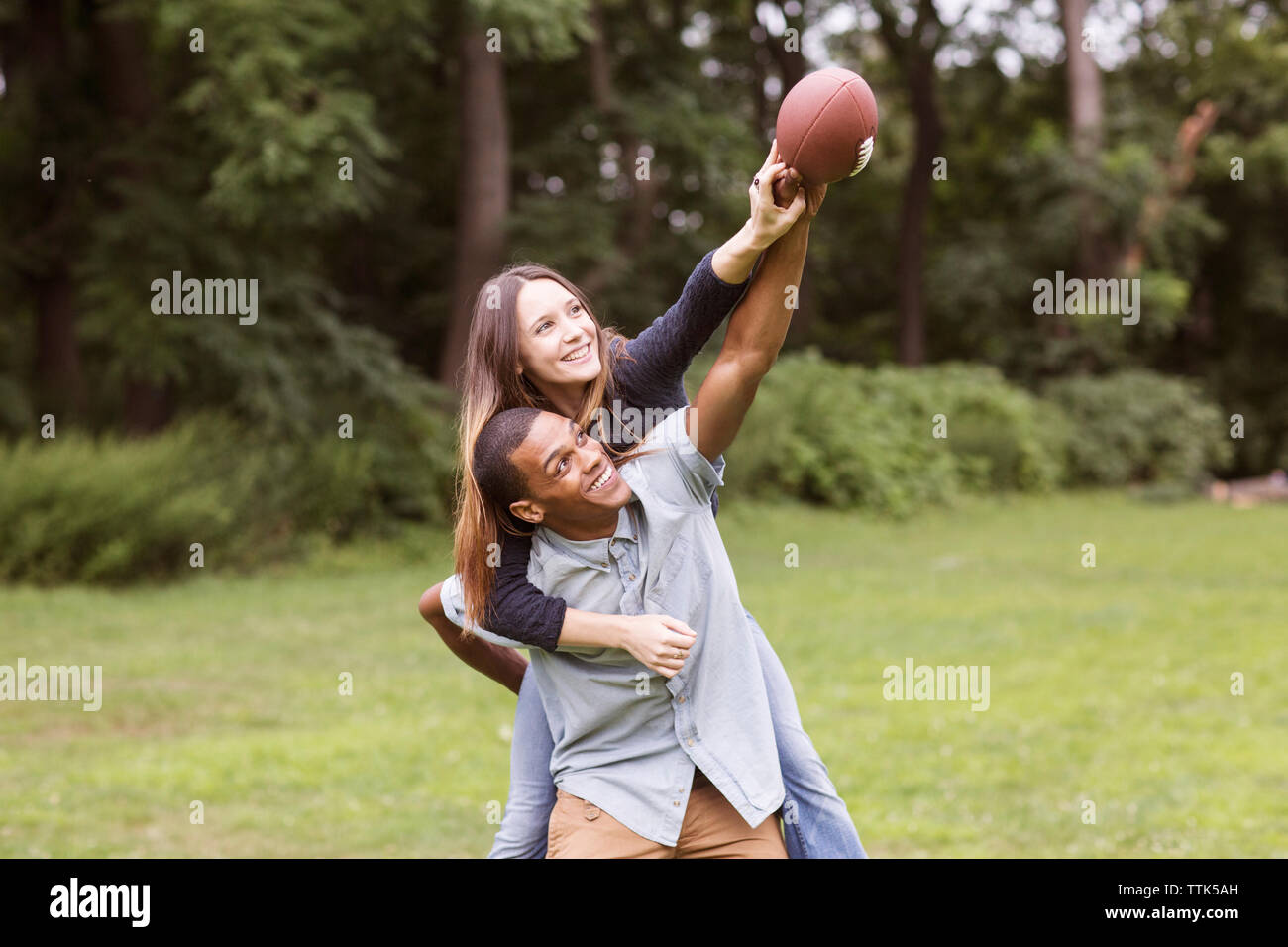 Man piggybacking woman while playing football on field Stock Photo - Alamy