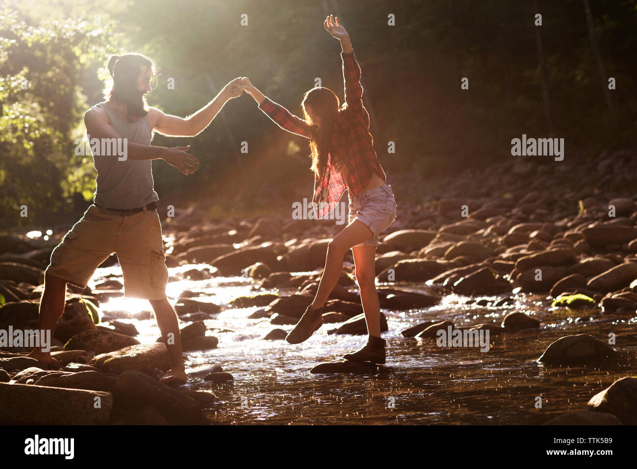 Boyfriend holding girlfriend while crossing stream in forest Stock Photo