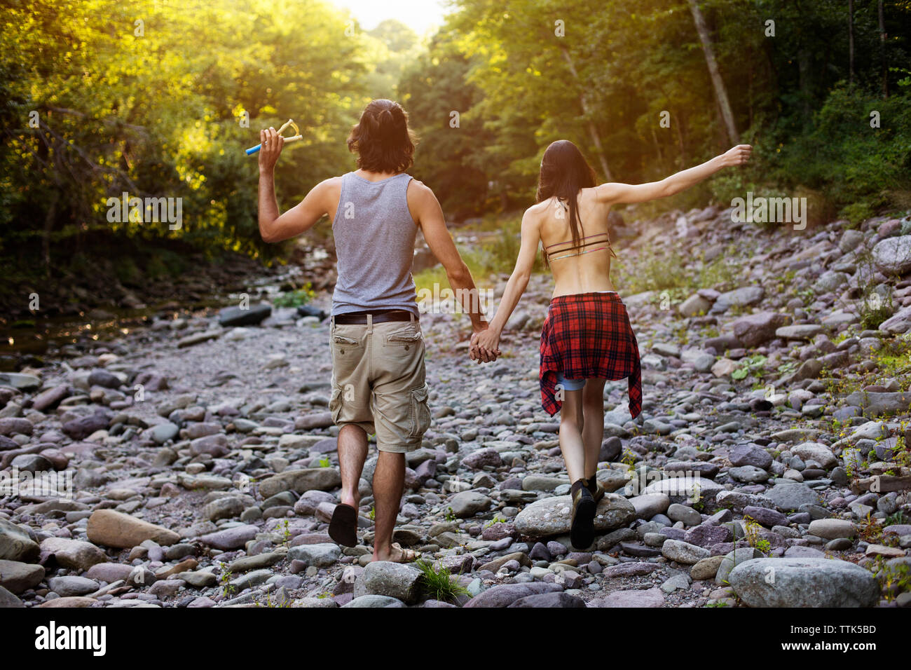 Rear view of couple holding hands while walking on rocks in forest Stock Photo
