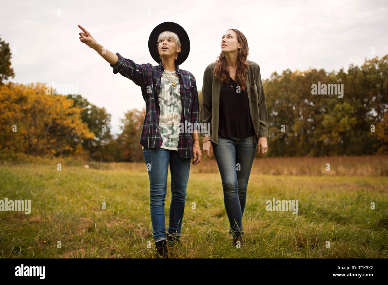 Young woman pointing and showing friend while walking on field Stock Photo