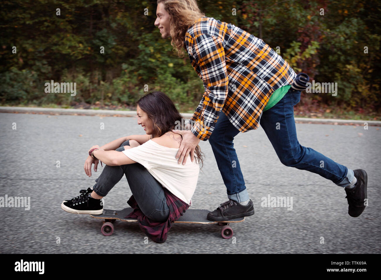 Man pushing woman sitting on skateboard at street Stock Photo