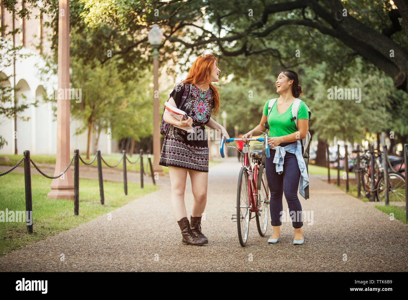 Happy friends walking with bicycle on footpath Stock Photo