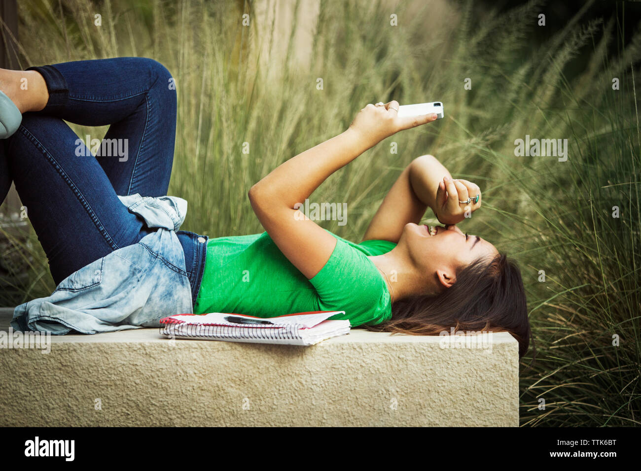 Happy woman using mobile phone while lying on concrete bench Stock Photo