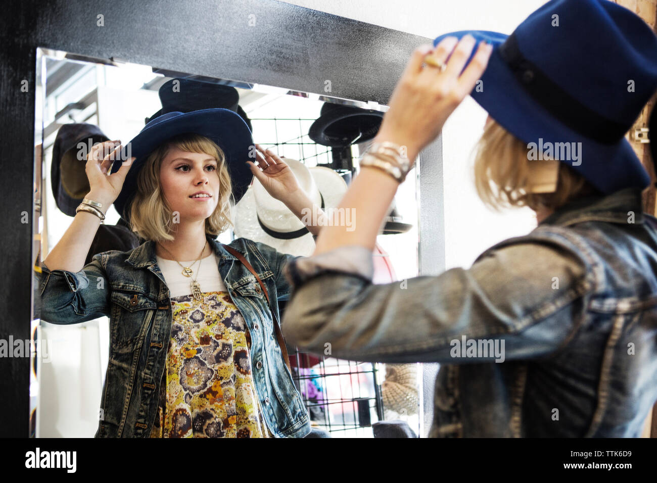 Woman trying on hat while standing in front of mirror Stock Photo