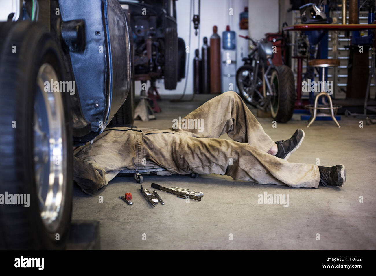 Side view of mechanic on creeper dolly while working under car in auto  repair shop Stock Photo - Alamy