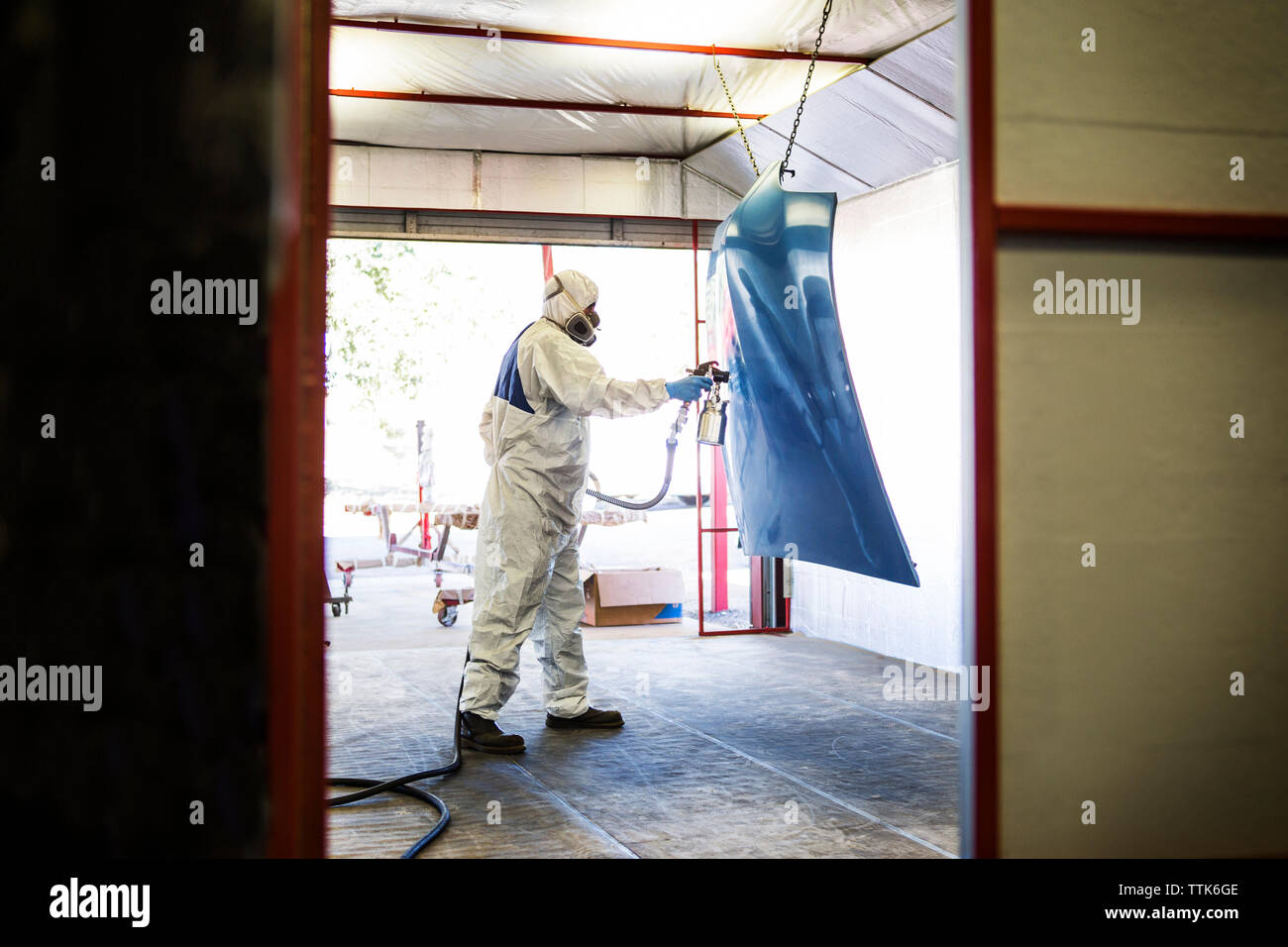 Mechanic in protective workwear painting vehicle part in auto body shop Stock Photo