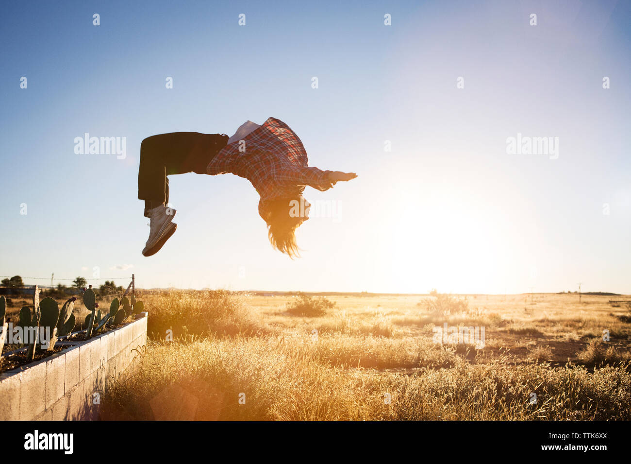 Side view of man doing somersault on field during sunset Stock Photo