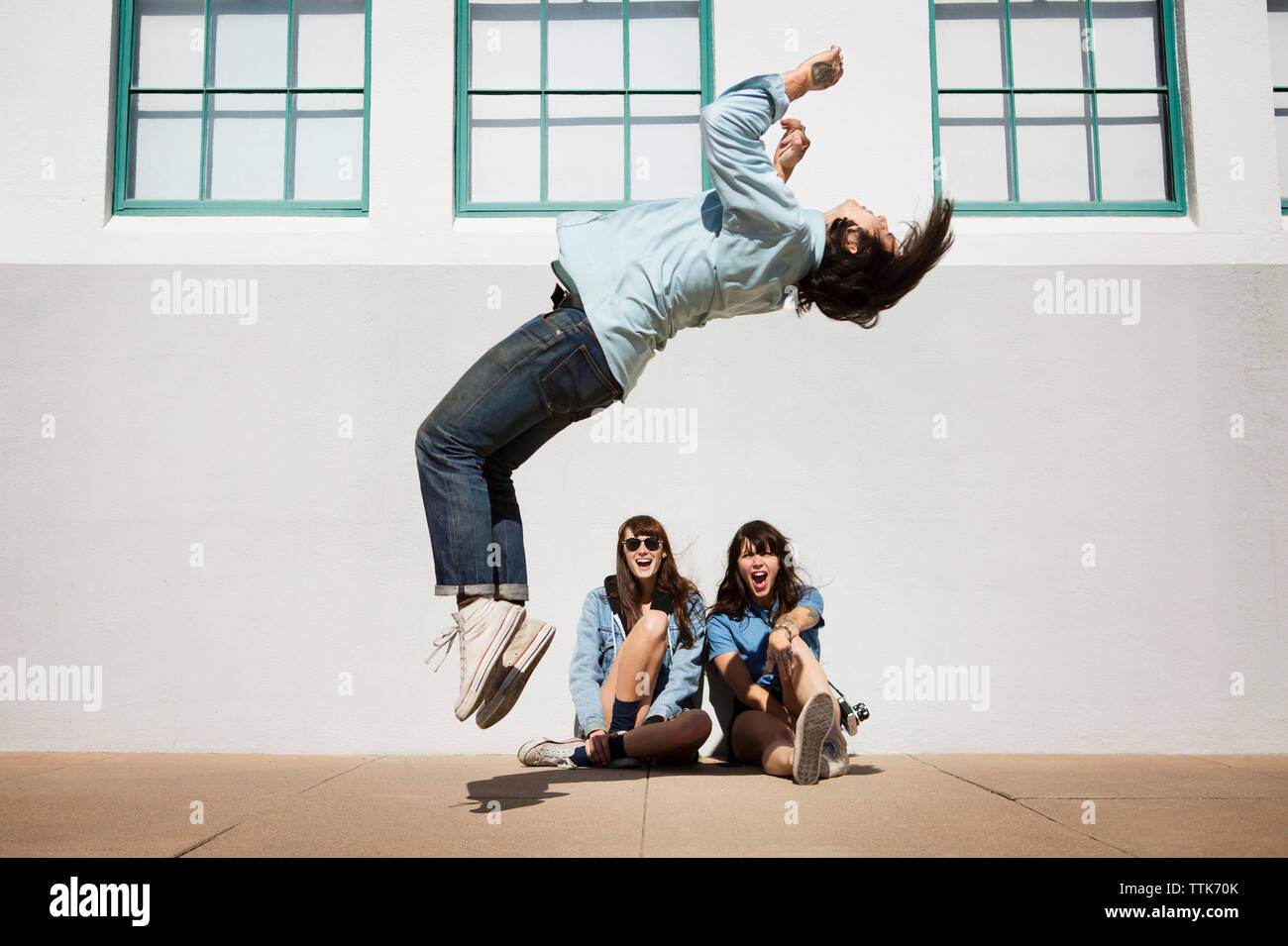 Man doing somersault while friends sitting against wall Stock Photo