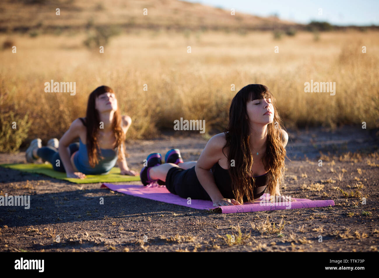 Young women practicing yoga on exercise mat in field Stock Photo