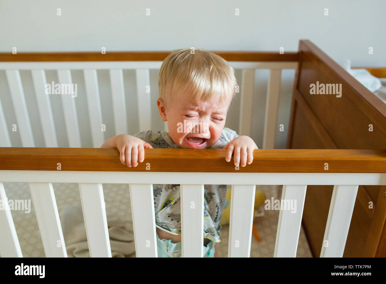 Baby Boy Crying While Standing In Crib At Home Stock Photo