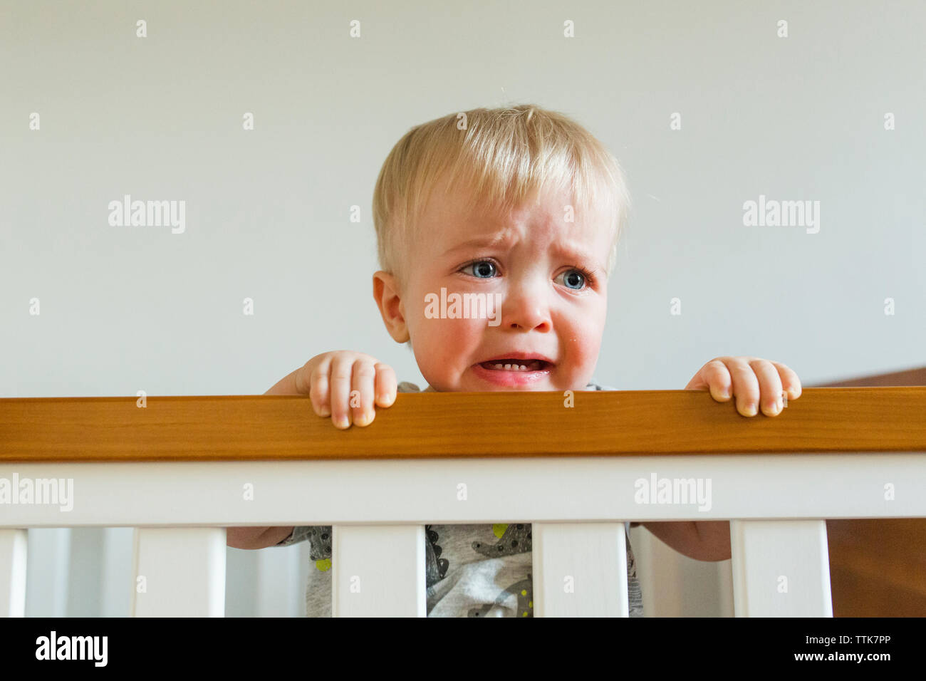 Cute baby boy looking away while crying in crib at home Stock Photo Alamy