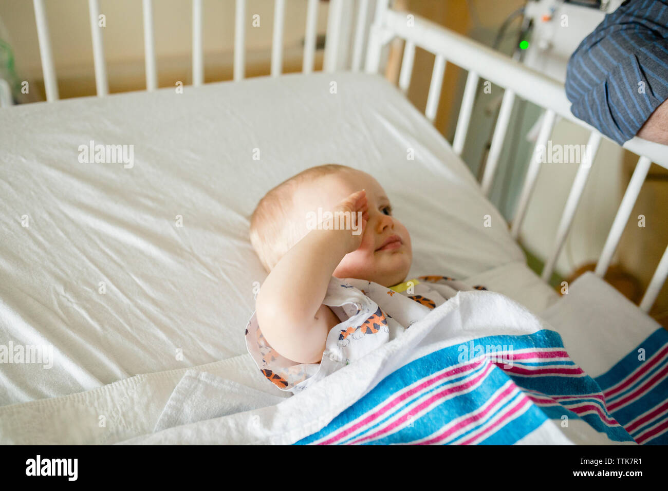 Sick baby boy rubbing eye while lying in hospital crib Stock Photo