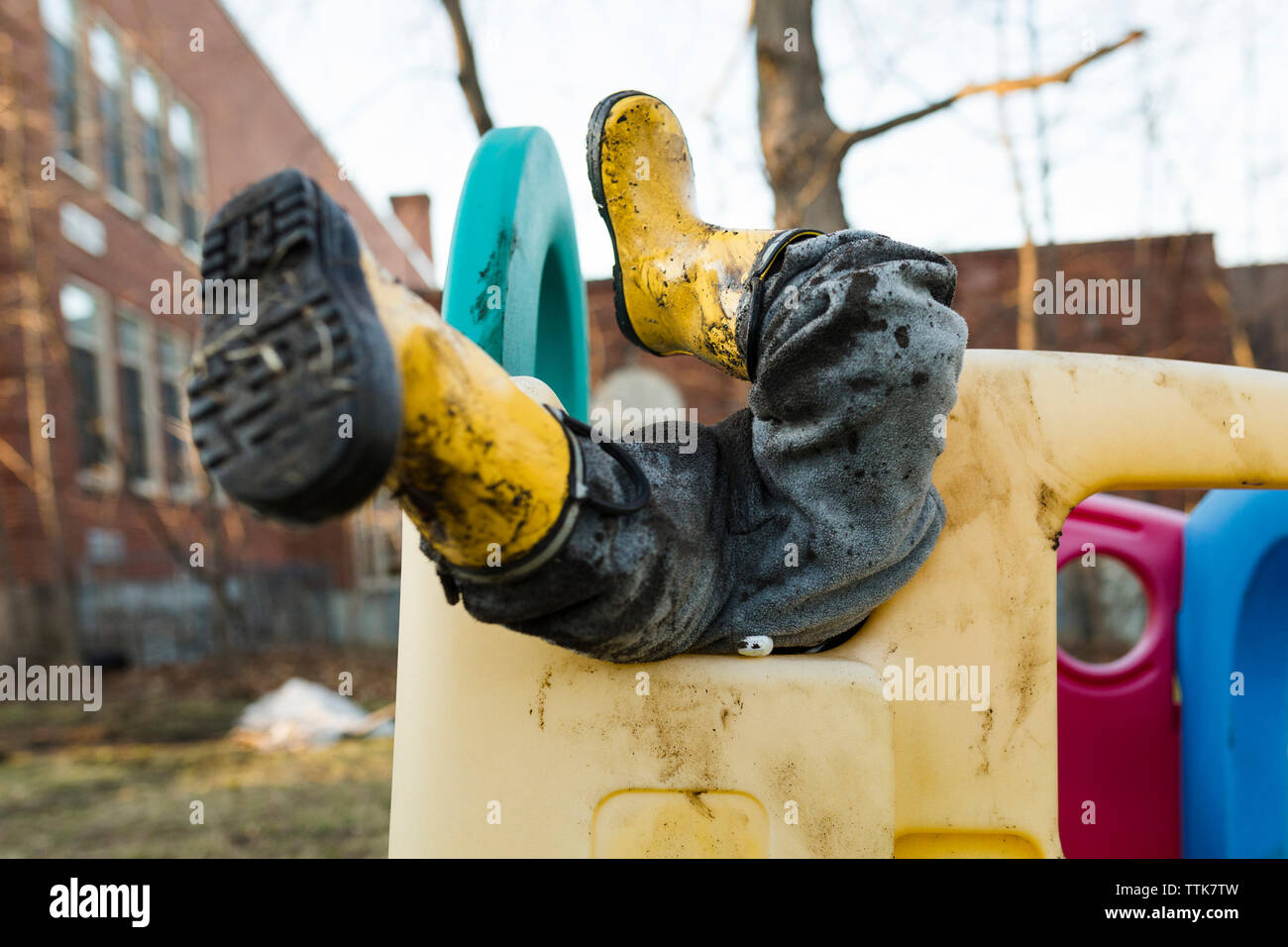 Low section of playful boy wearing muddy rubber boots while playing on outdoor play equipment at playground Stock Photo