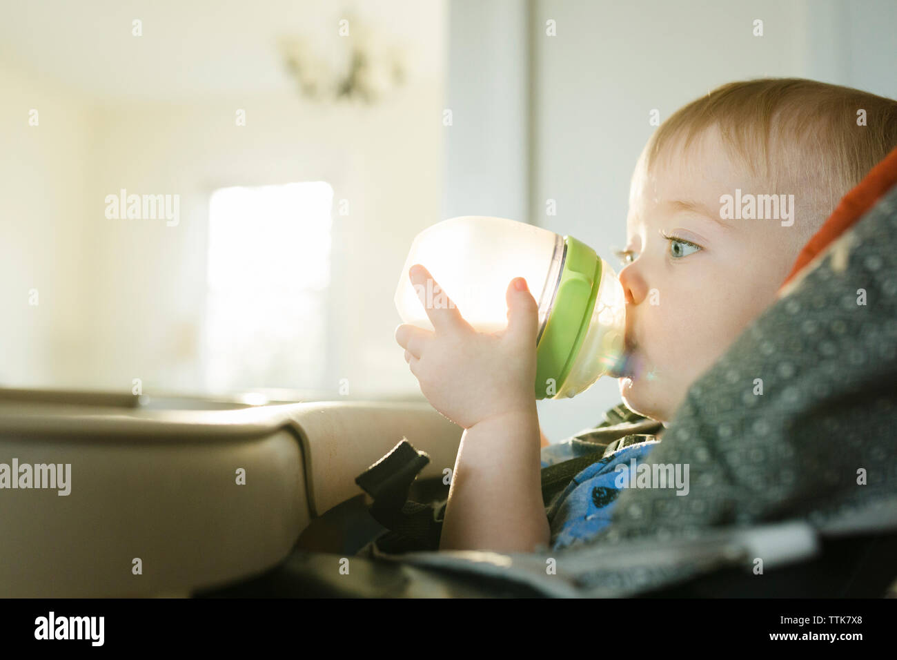 Boy feeding milk to brother from baby bottle while sitting on sofa at home  Stock Photo - Alamy