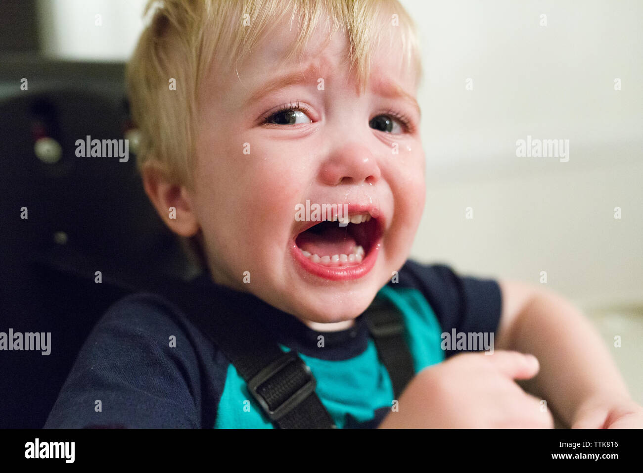 Close-up portrait of angry baby boy crying while sitting on high chair at home Stock Photo
