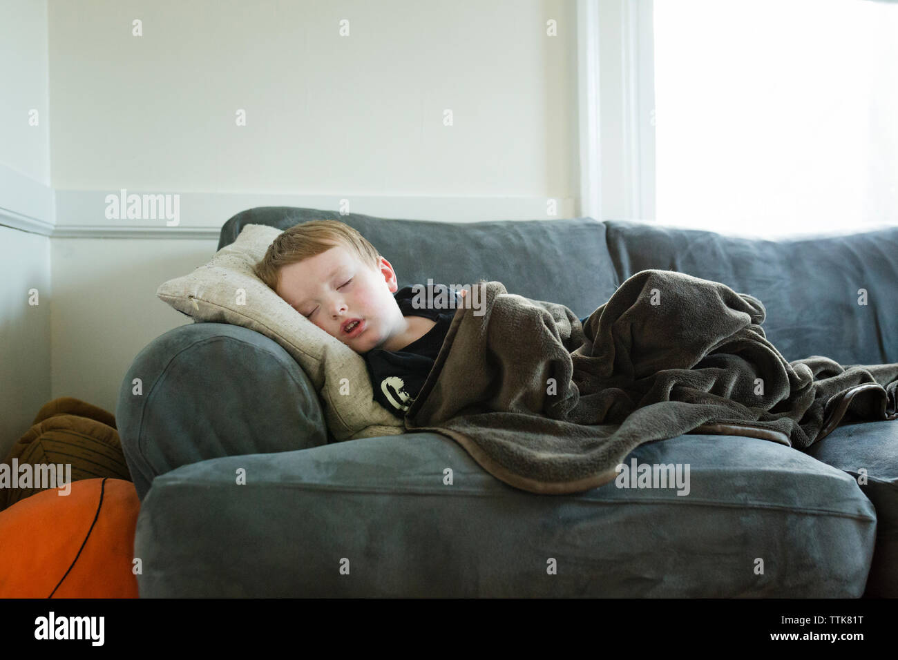 Preschool age boy naps on couch covered with a blanket Stock Photo