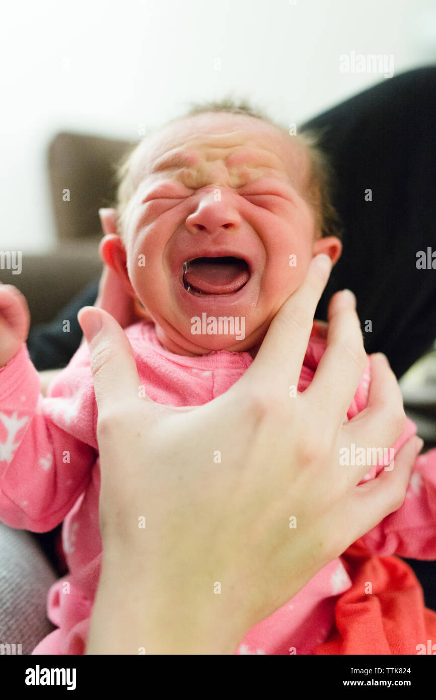 Multiracial newborn baby girl cries while being held upright by mother Stock Photo