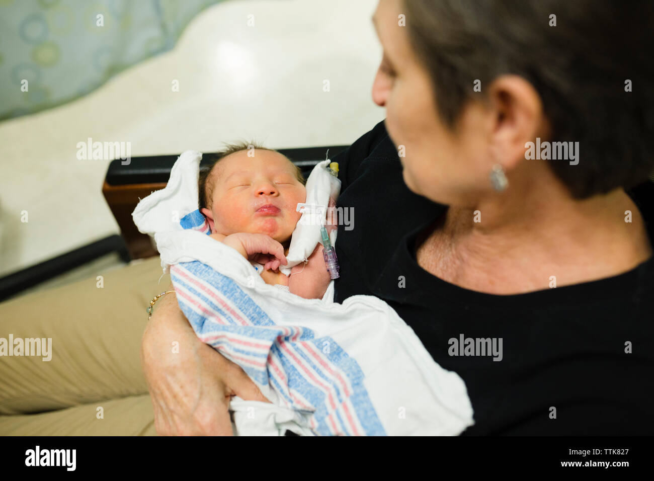 Grandma holds newborn baby grandchild in hospital room Stock Photo