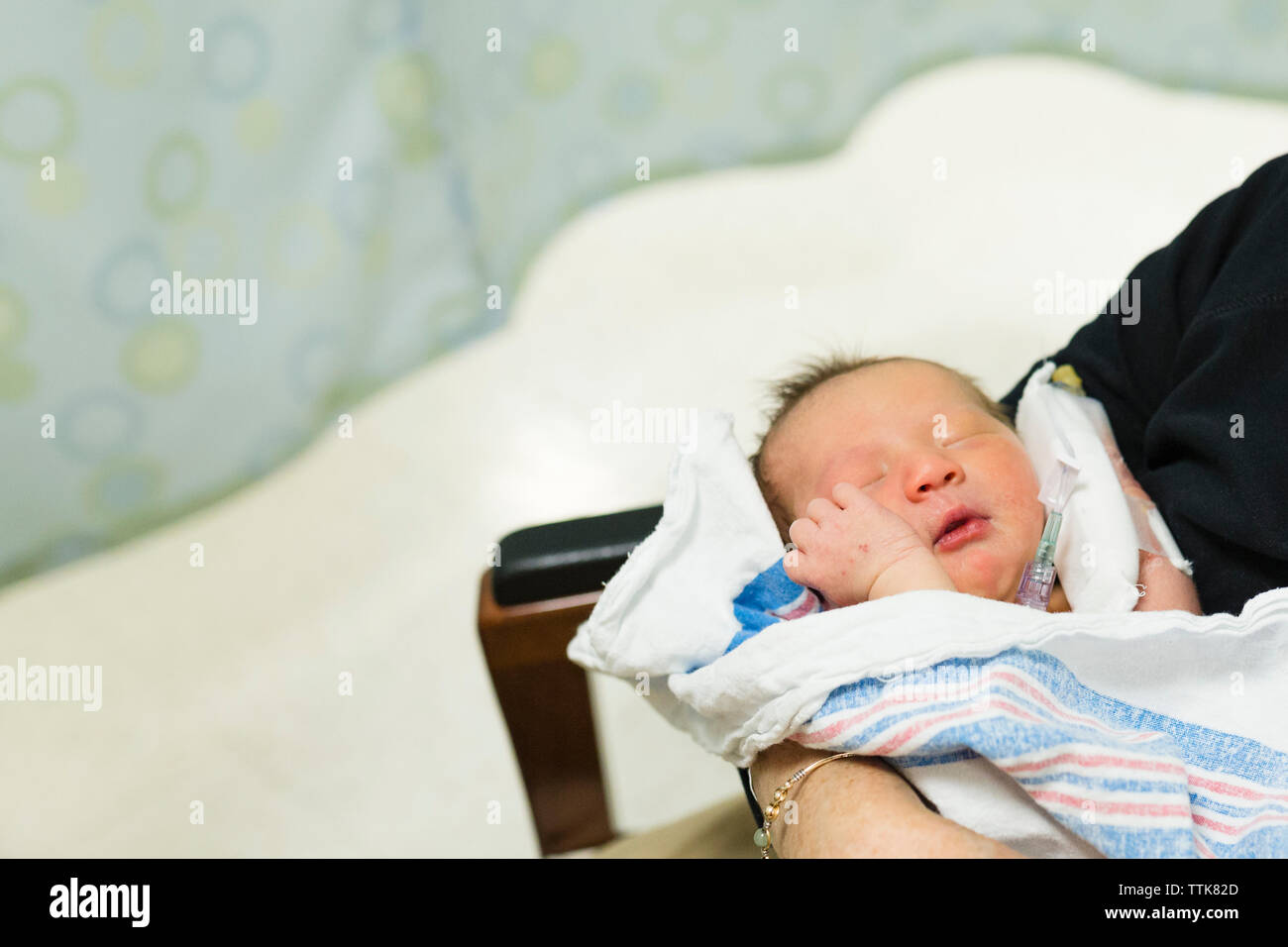 Newborn baby with hands near face being held in hospital room Stock Photo
