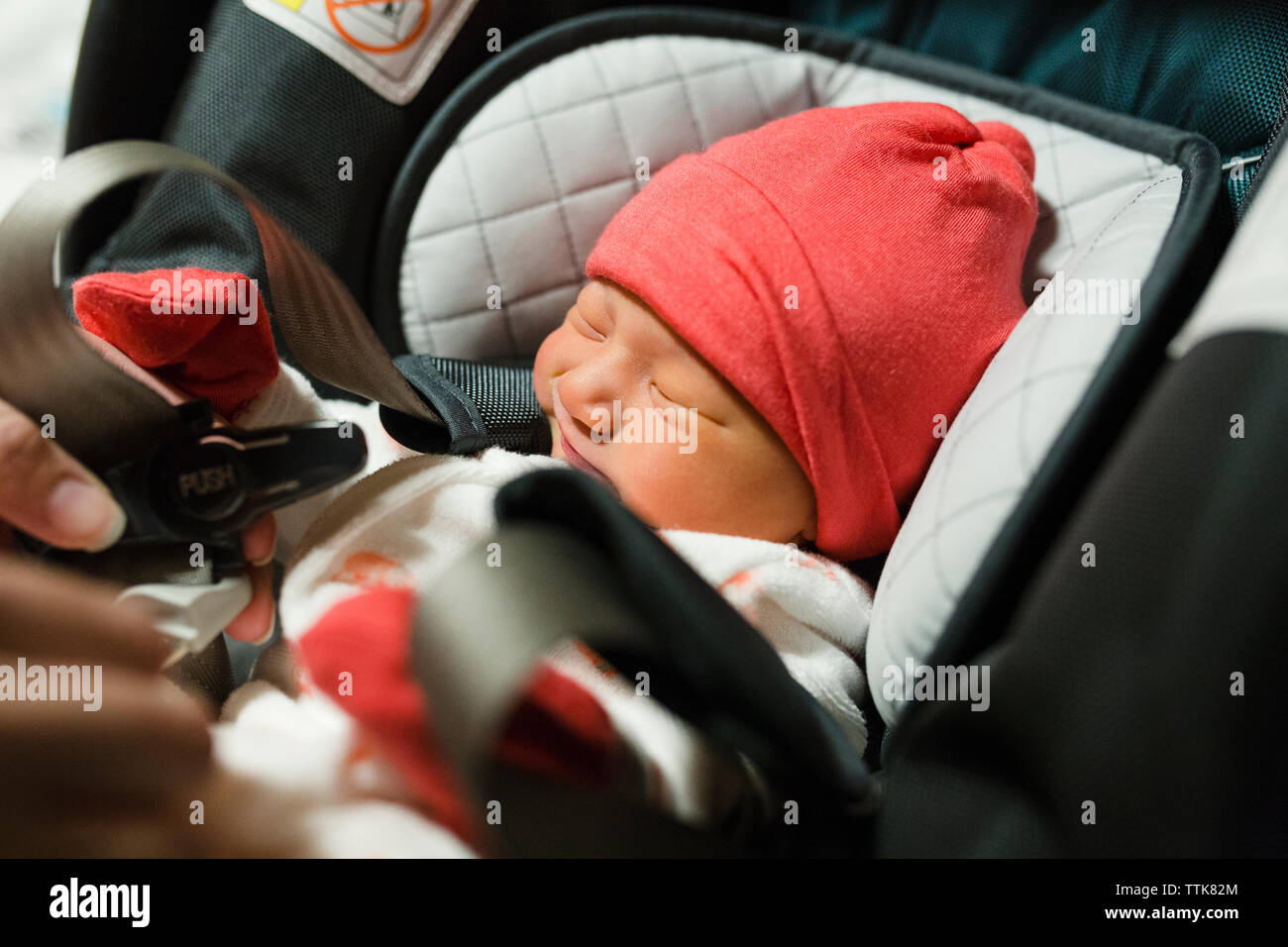 Newborn baby girl getting strapped into carseat wearing pink hat Stock Photo