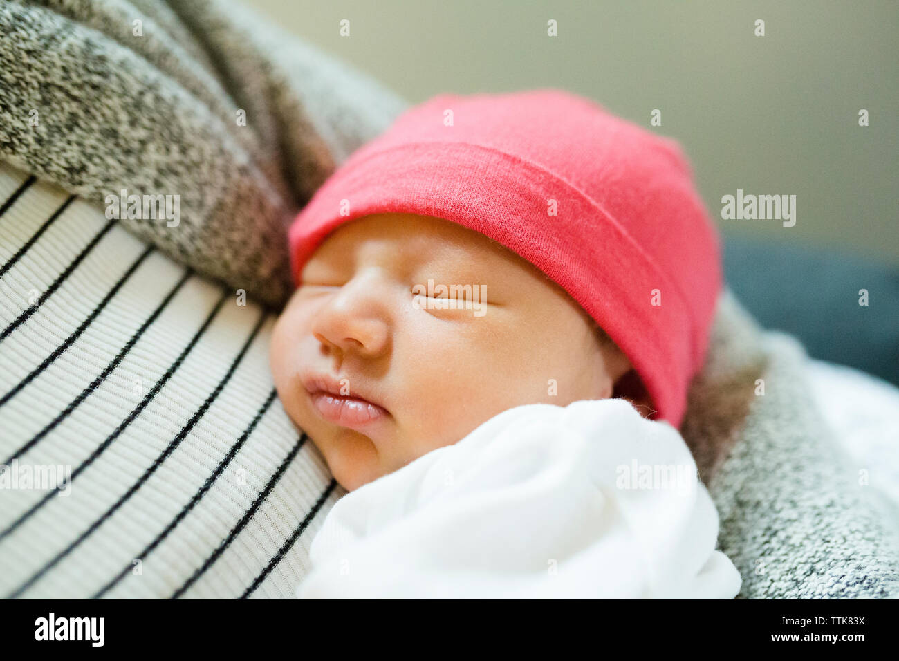 Sleeping newborn baby girl being held in mother s arms wearing hat