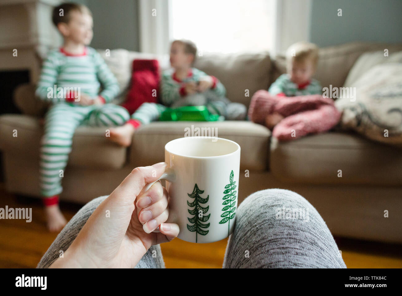 Mom holding coffee mug watches three kids open Christmas stockings Stock Photo