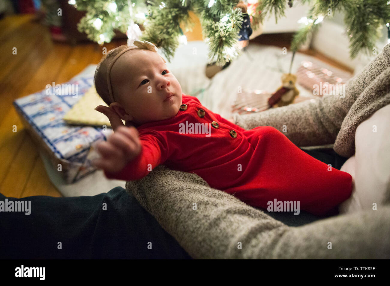 Baby girl wearing bow and red looks up at mom next to Christmas tree Stock Photo