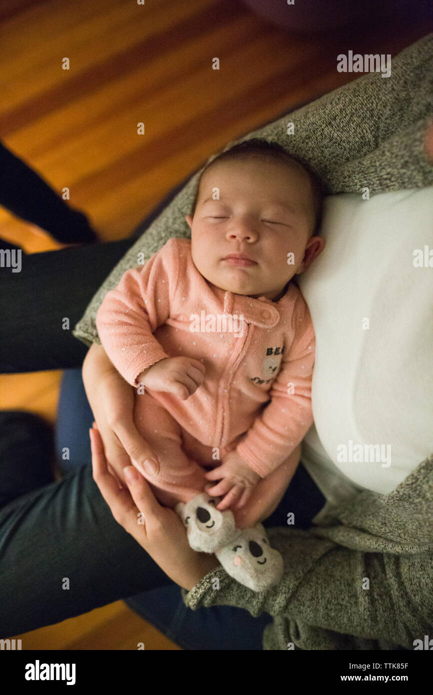 Newborn baby girl sleeps peacefully in mother's arms indoors Stock Photo