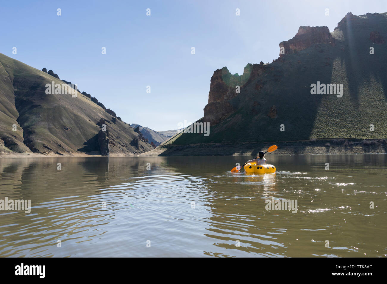 Rear view of hiker paddling inflatable boat at Owyhee River against clear sky Stock Photo