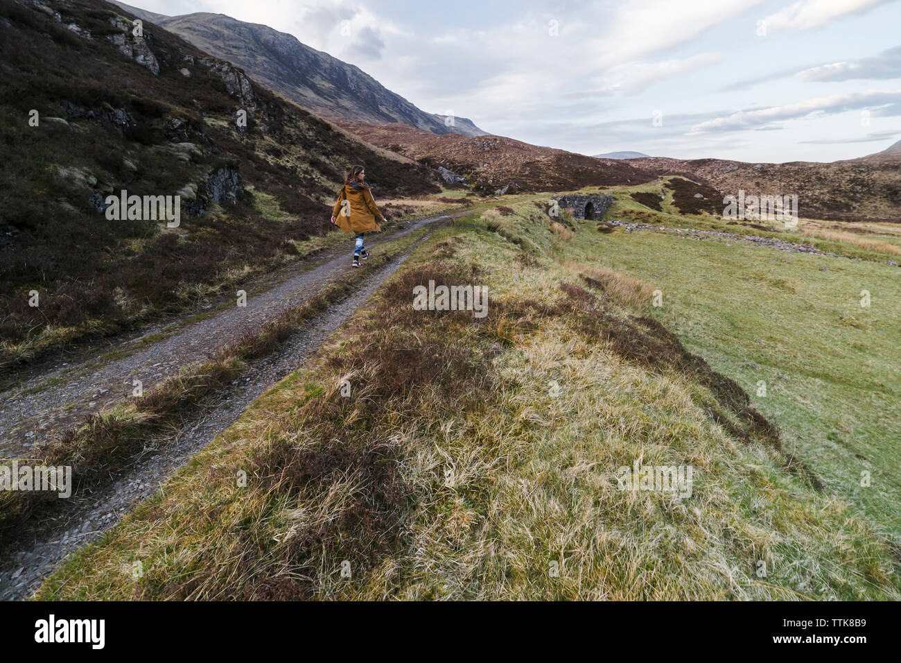 Rear view of woman walking on footpath amidst field and mountains Stock ...