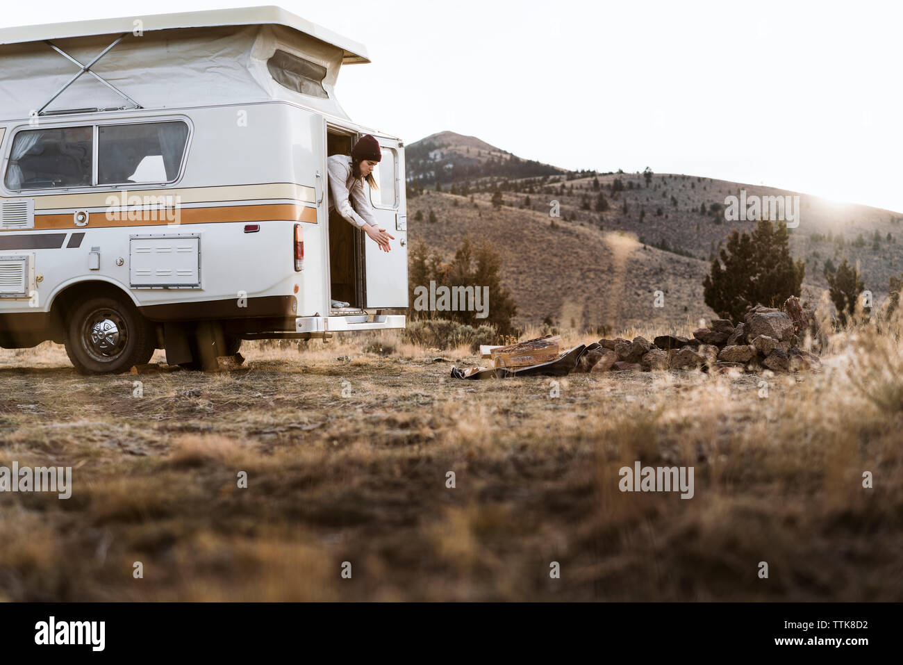 Woman dusting hands while standing in camper van on field against clear sky Stock Photo