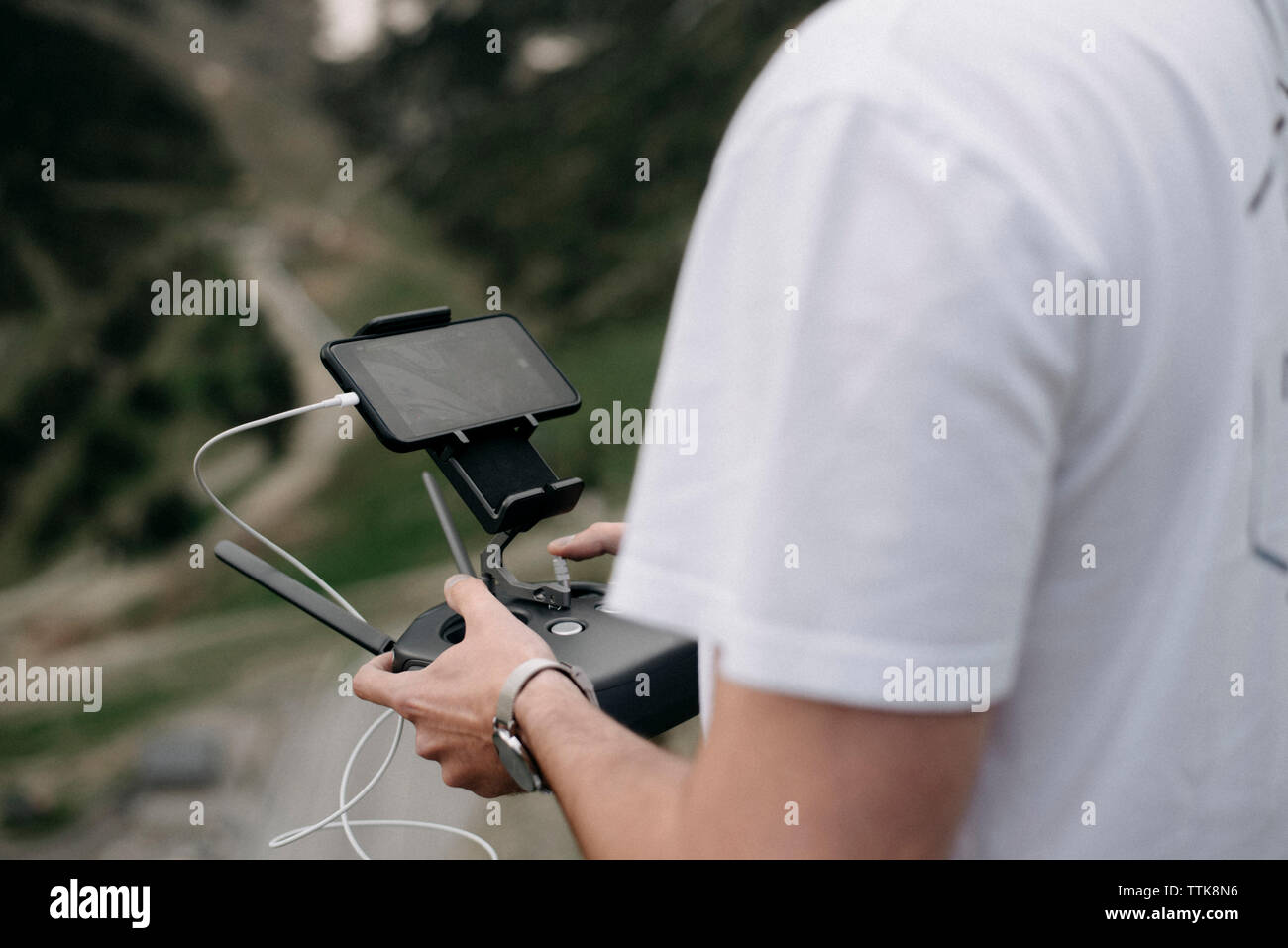 Midsection of man using mobile phone with remote control while standing outdoors Stock Photo