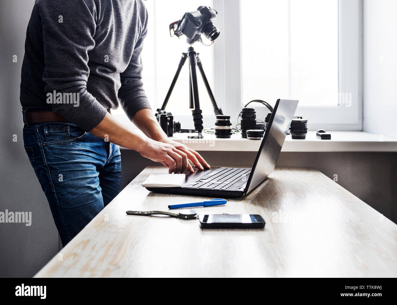 Midsection of man using laptop on table against window Stock Photo