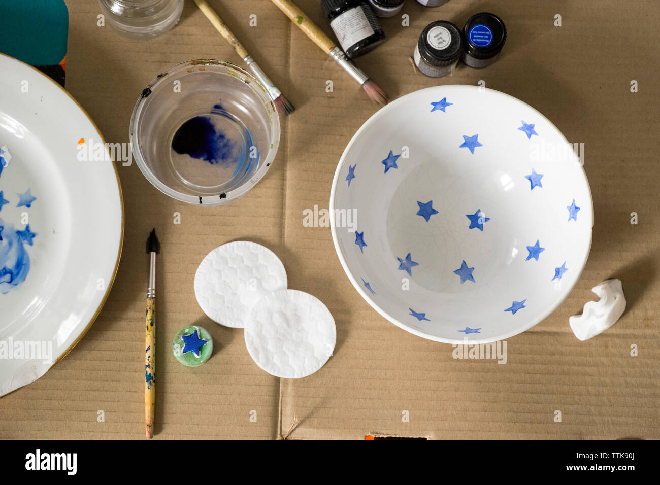 Overhead view of watercolor paints and brushes with bowls on cardboard Stock Photo