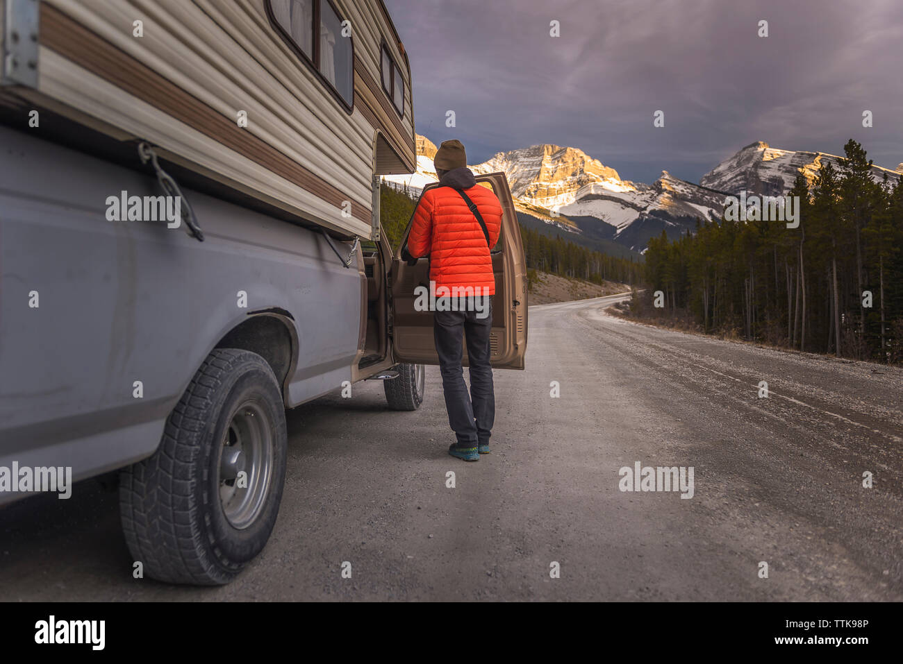 Man standing next to camper truck in front of sunset in mountains Stock Photo