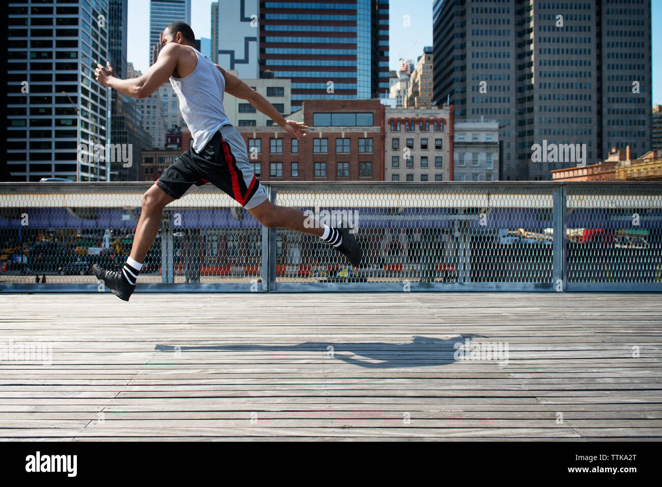 Side view of man jumping on boardwalk against modern buildings Stock Photo